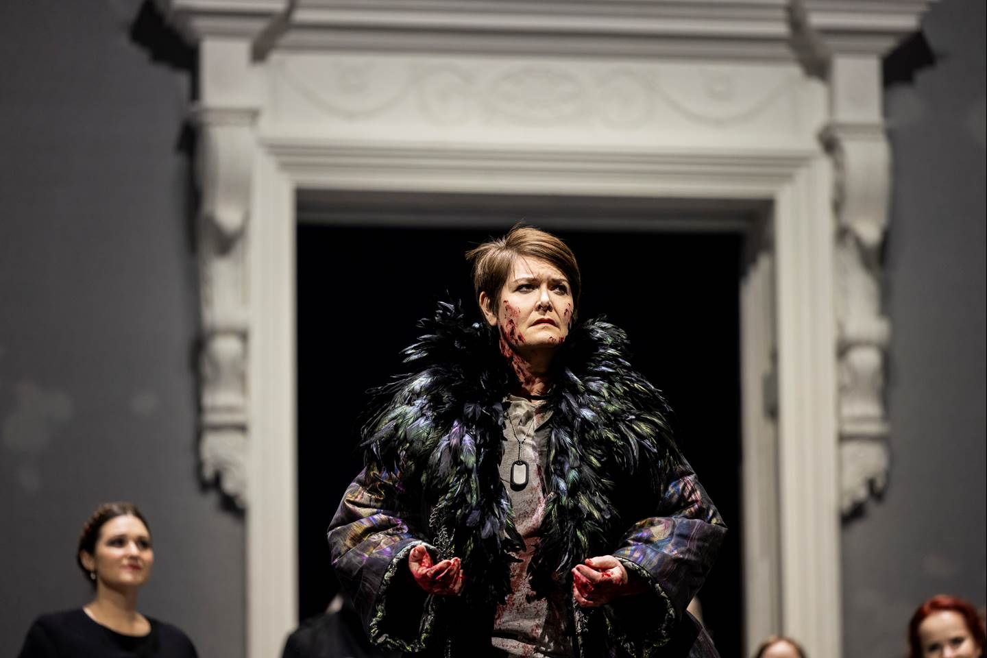 A woman in a feathered jacked with blood all over from the opera Idomeneo