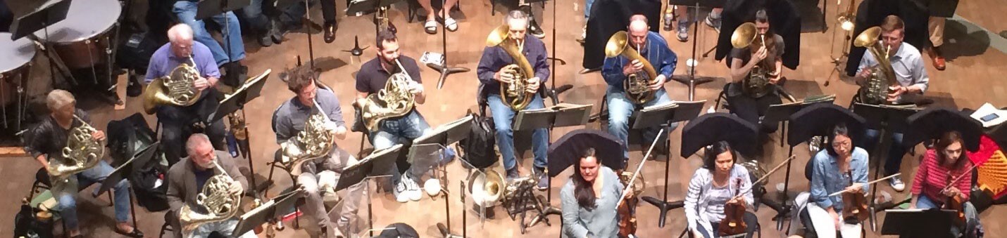 The nine pit horns of the San Francisco Opera Orchestra, five playing French horn on the left and four Wagner tubas on the right.