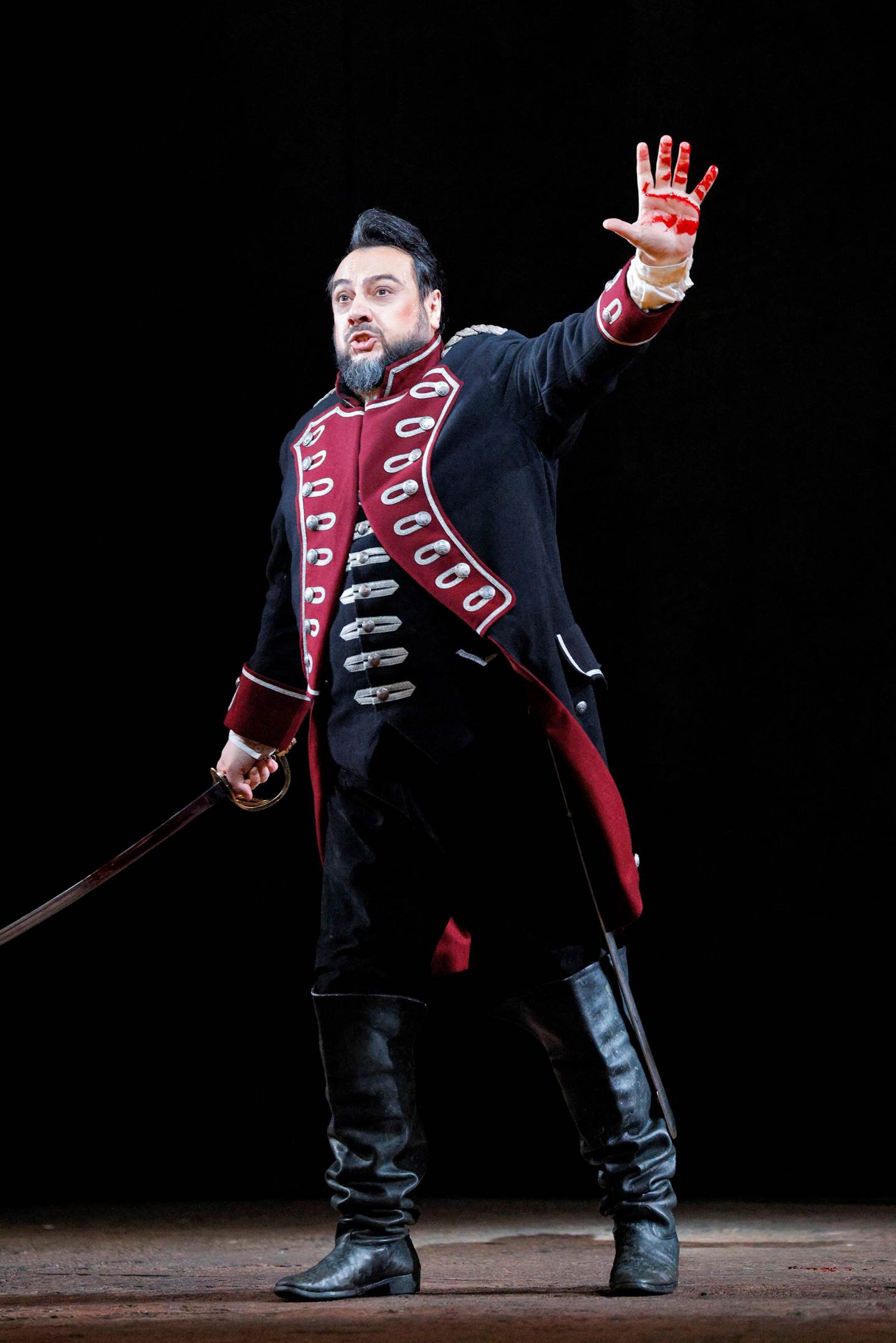 man on stage with sword in right hand and a bloody left hand raised to show the audience while singing