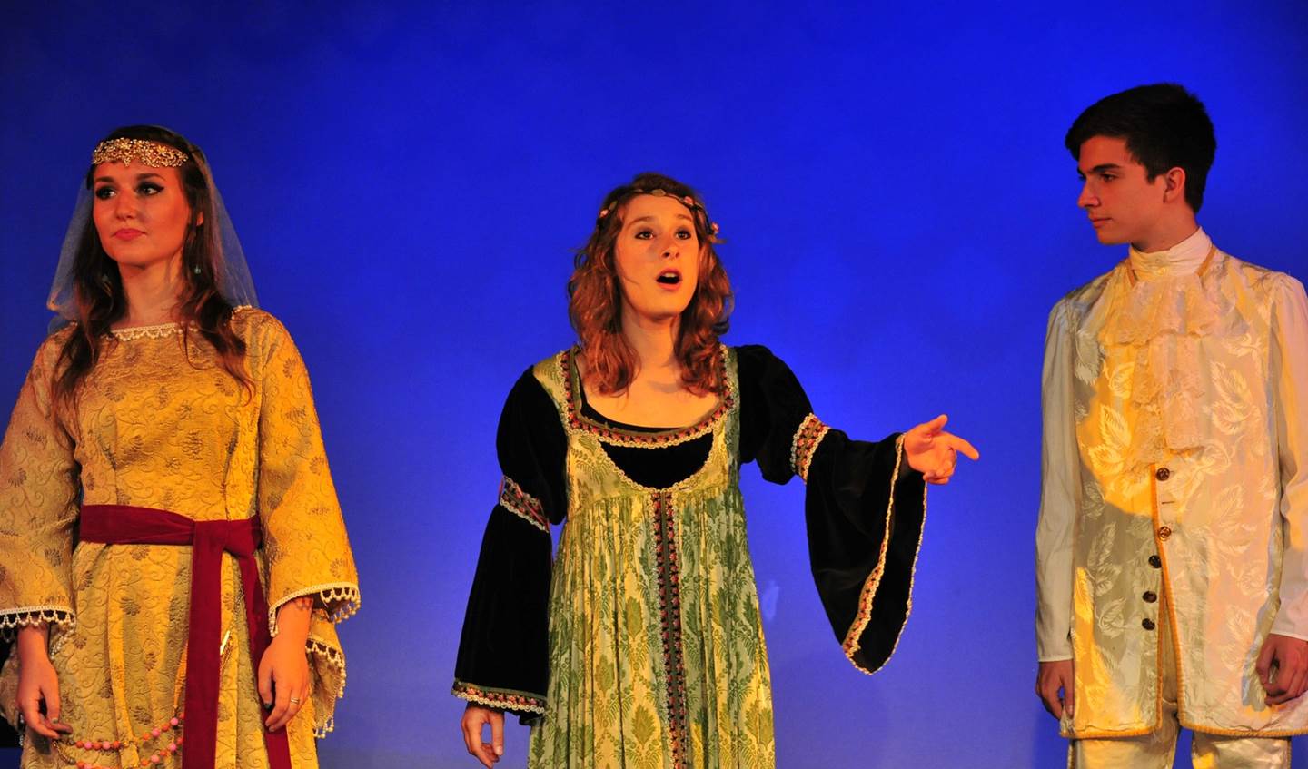 A young woman is singing with her hand outstretched forward while a young man looks at her and another young lady is looking off into the distance.