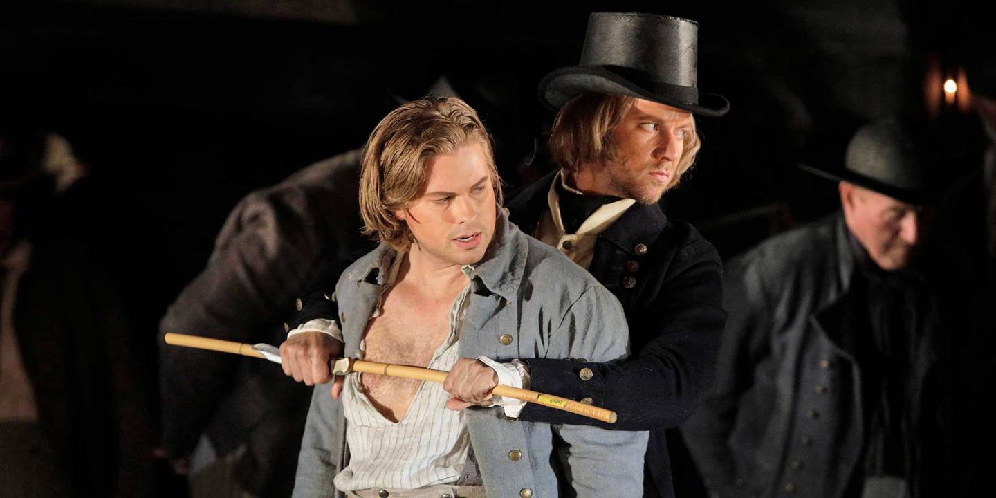  Billy Budd being held back with a man holding a stick across his chest