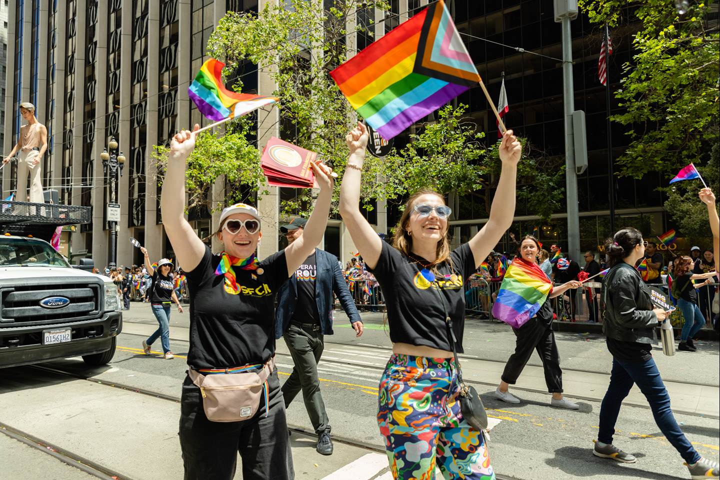 SFO cast members walking in the 2023 Pride Parade waving colorful flags